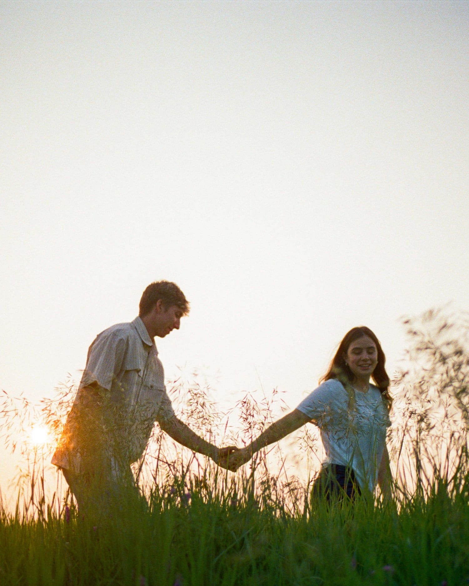 Couple holding hands and walking through grass at sunset in Bowmanville.