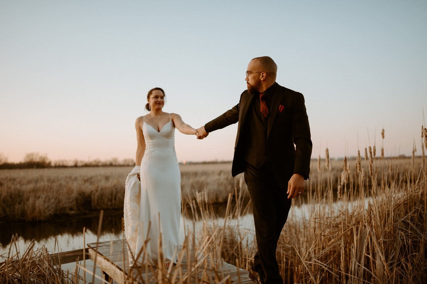Bride and groom walking through tall grass at Prince Edward County wedding.